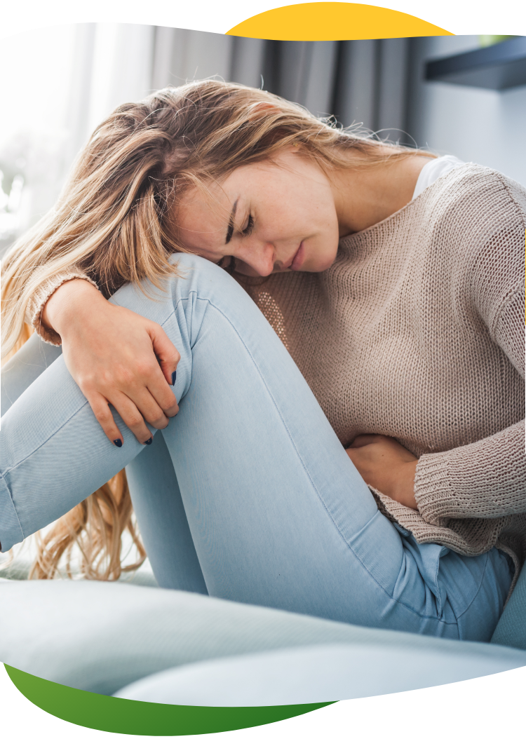Djevojka koja pati od nadutosti zbog menstruacije sjedi zgrčena na podu i drži se za stomak lijevom rukom